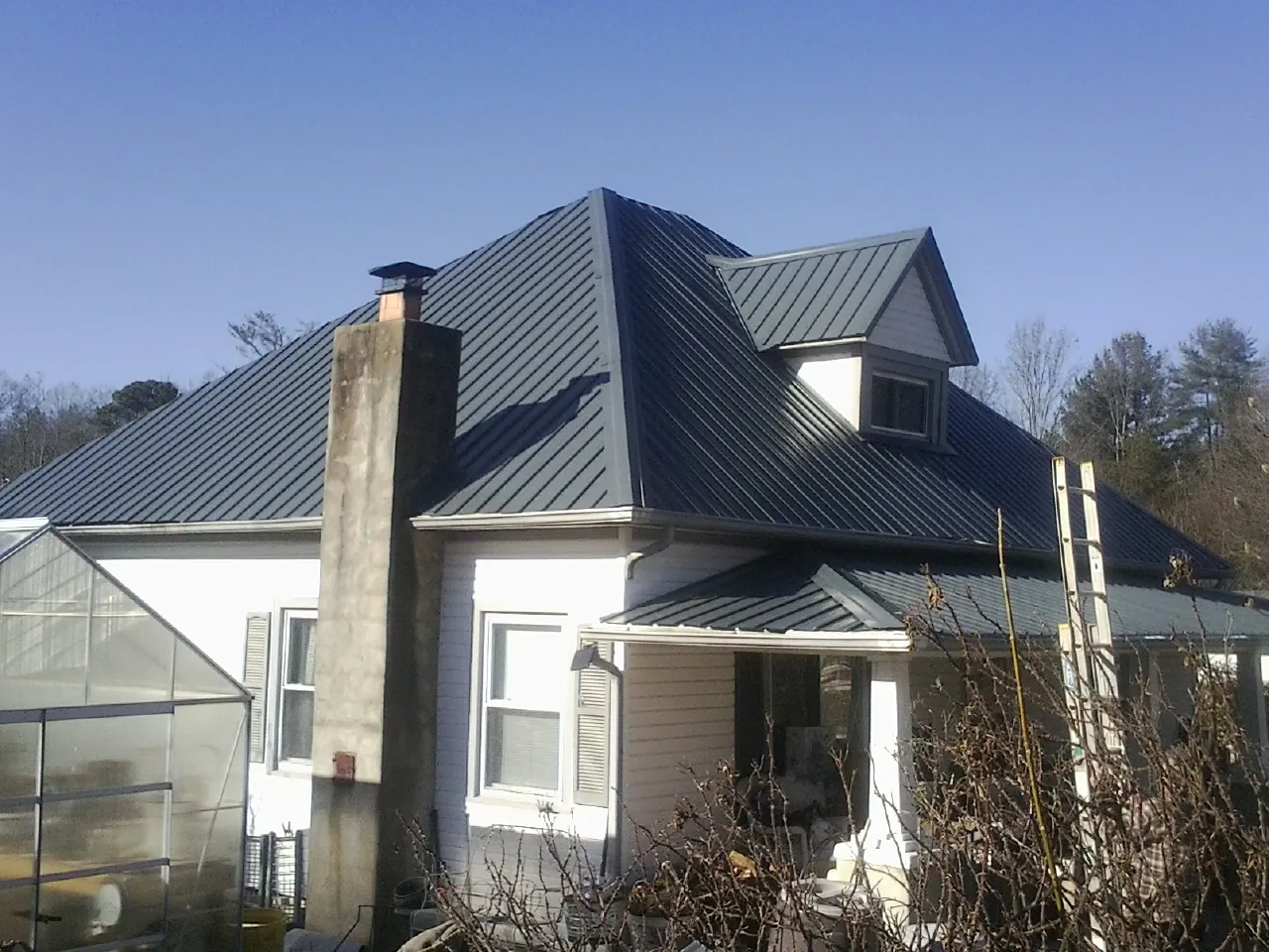 Dark blue standing seam metal roof on a white farmhouse with dormer — Slate & Tile Roof Repair by Roofing Brothers in Bartow
