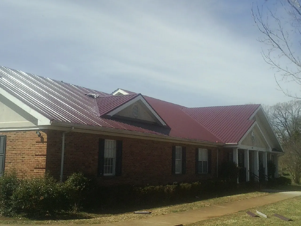 Red metal roof with gabled entries on a long brick building, from a Hail Damage Roof Repair job in Bartow