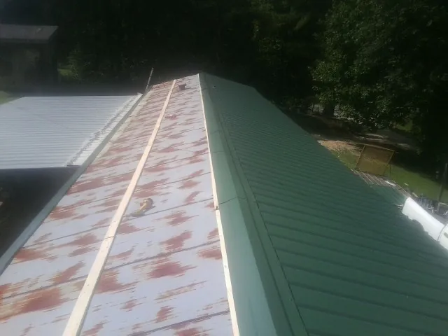 Old rusted panels beside newly installed green metal roofing — Wind Damage Roof Repair by Roofing Brothers in Bartow
