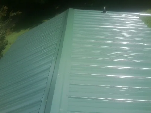 New green metal panels meeting at the ridge of a roof — Flat Roof Repair work by our crew in Bartow
