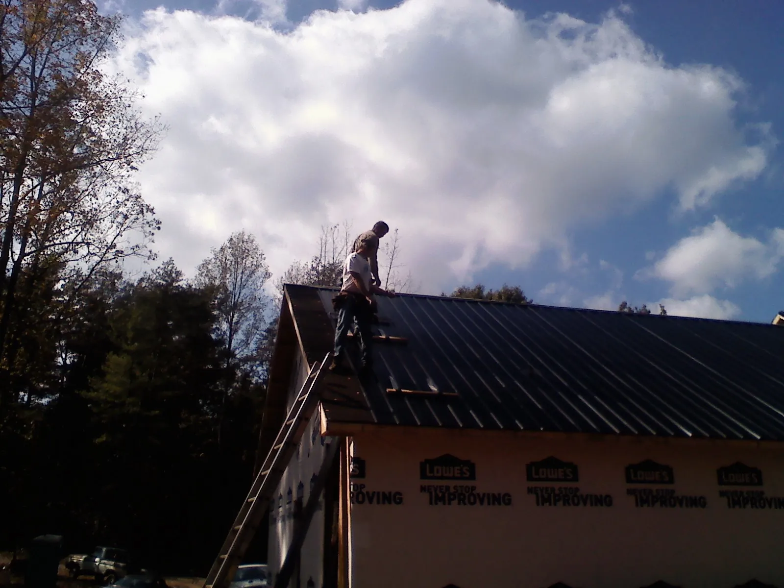 Roofer fastening dark metal panels high against a cloudy sky, from a Roof Inspection job in Bartow
