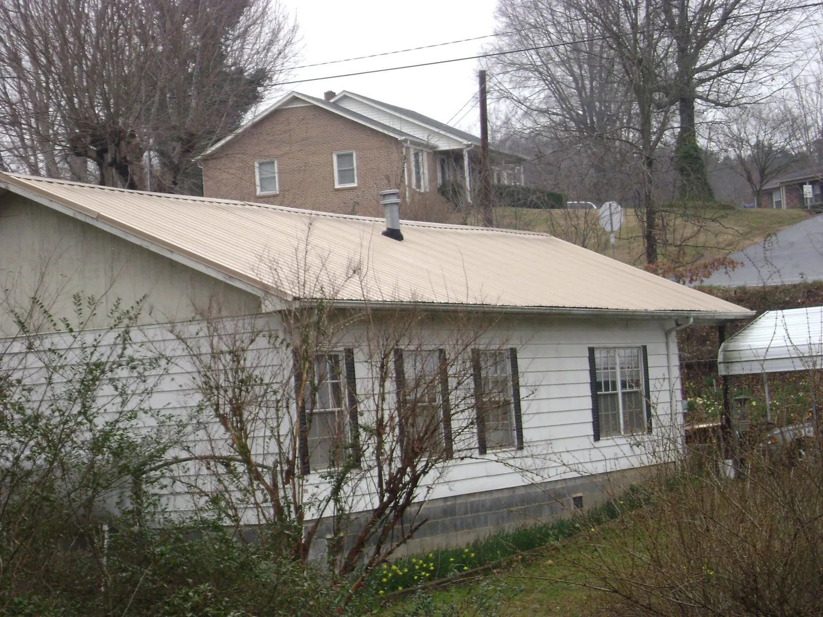 Tan metal roof on a white sided house set into a hillside — Commercial Roofing by Roofing Brothers in Bartow