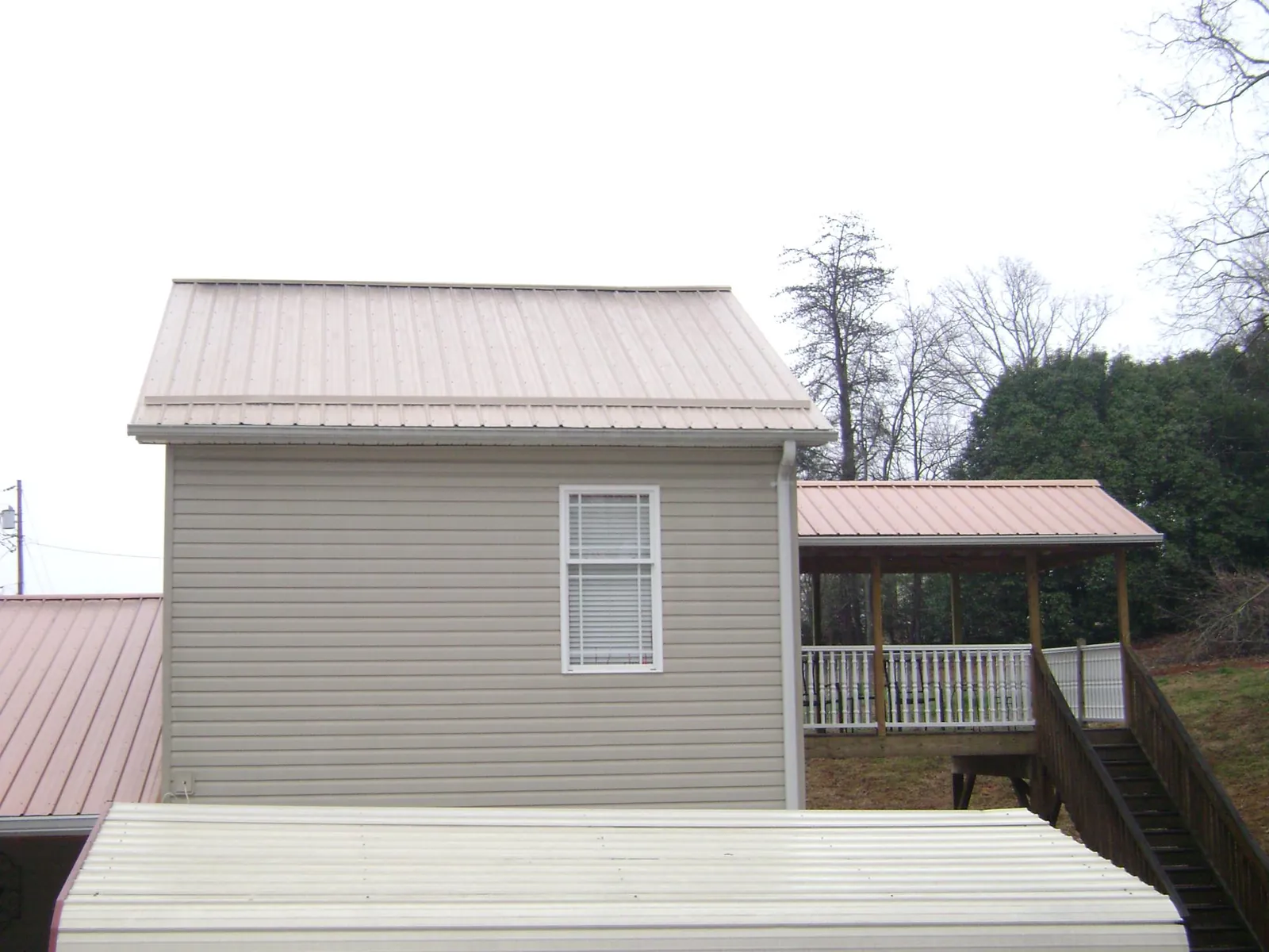 Tan metal roofs on a two story addition and attached porch, from a Roof Replacement job in Bartow